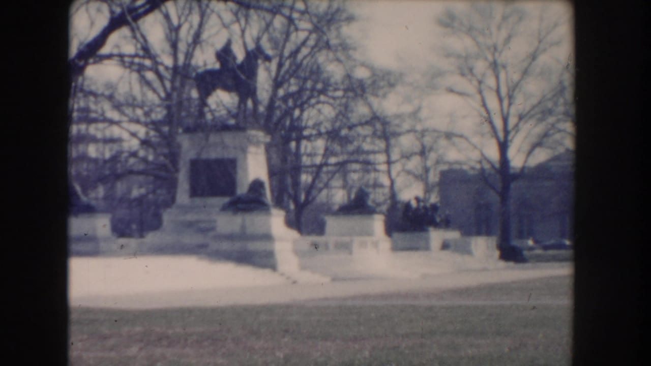 Equestrian statue on a stone monument framed by bare trees and low walls.