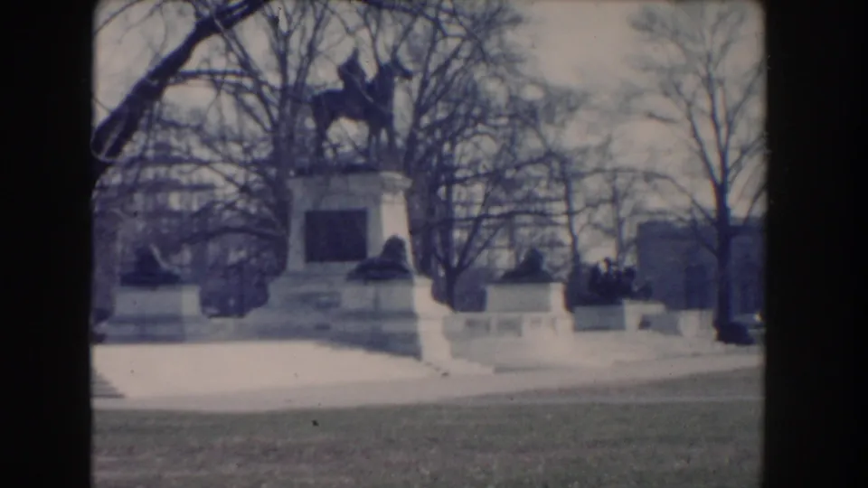 Washington DC home-movie frame showing the horse-and-rider monument, stone base, low walls, and winter trees.