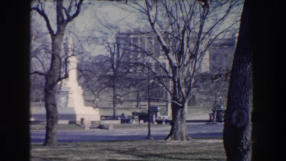 1960 Washington DC park view with a white monument, benches, leafless trees, paths, and a distant civic building.