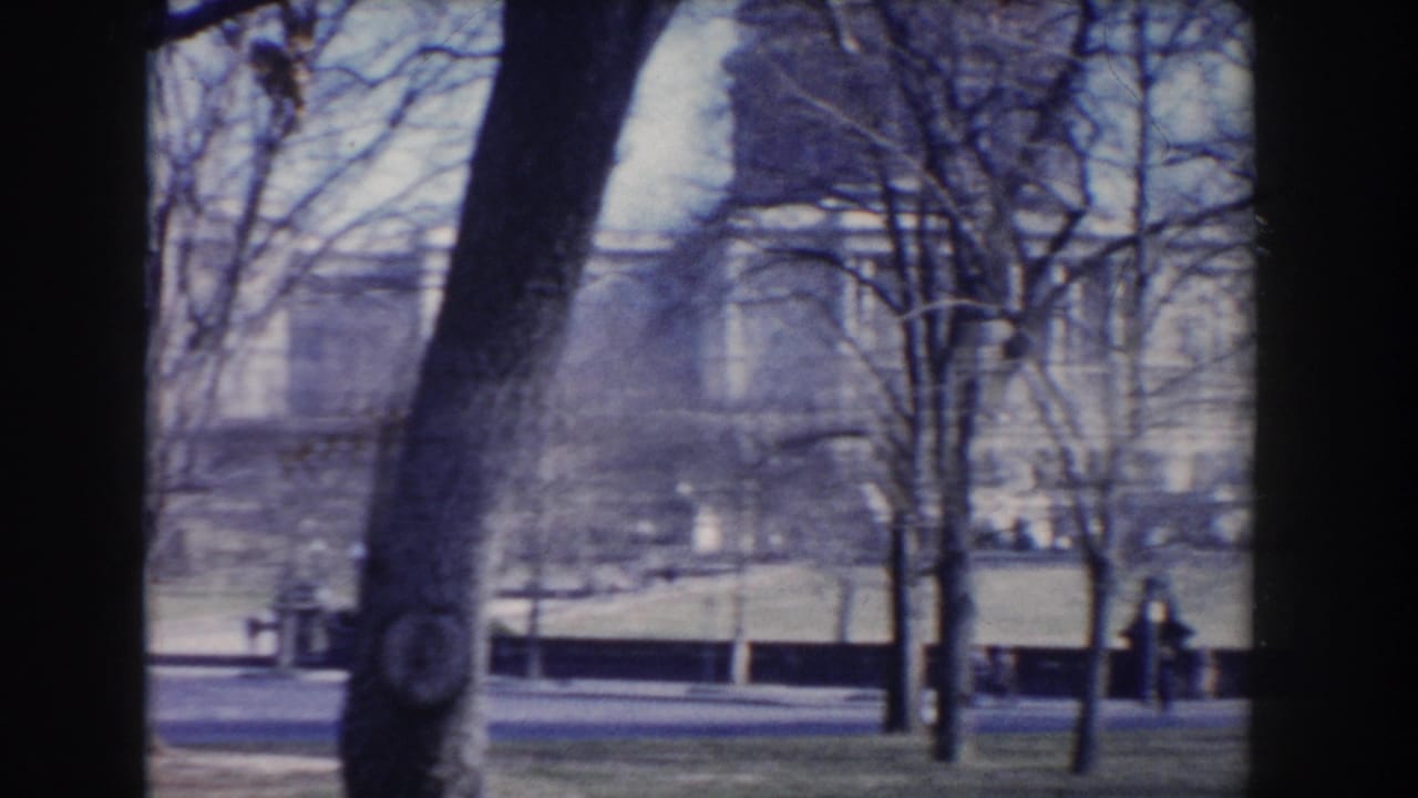 1960 8mm view of a Washington, DC park with bare trees, grass, a roadway, and distant civic structures.