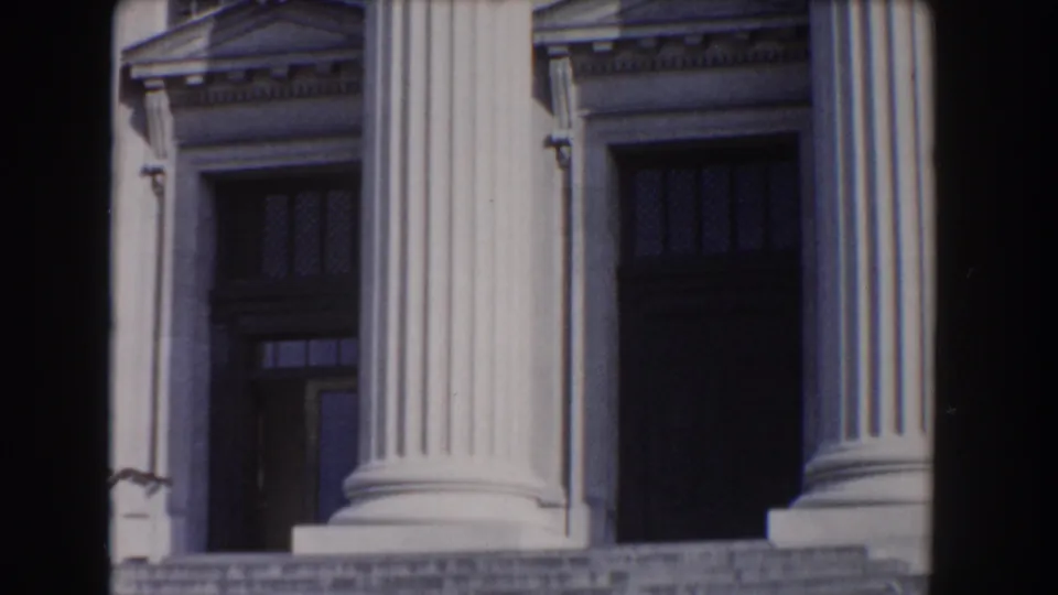 The camera lingers on tall fluted columns, dark entrance openings, and broad stone steps on a Washington, DC building exterior.