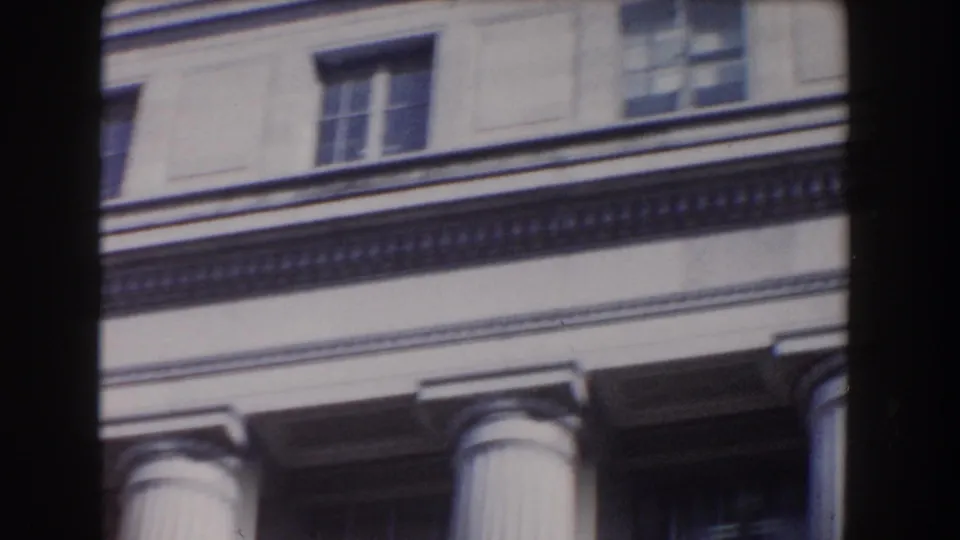 Close 8mm view of the upper portion of a Washington DC neoclassical building, including columns, windows, and ornamental trim.
