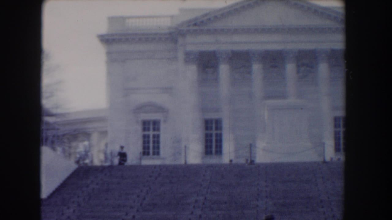 Distant guard standing on broad stone steps before a columned memorial building.