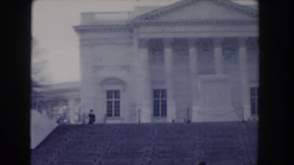 1960 Washington-area home-movie frame showing a distant military guard on the steps of a neoclassical memorial building.