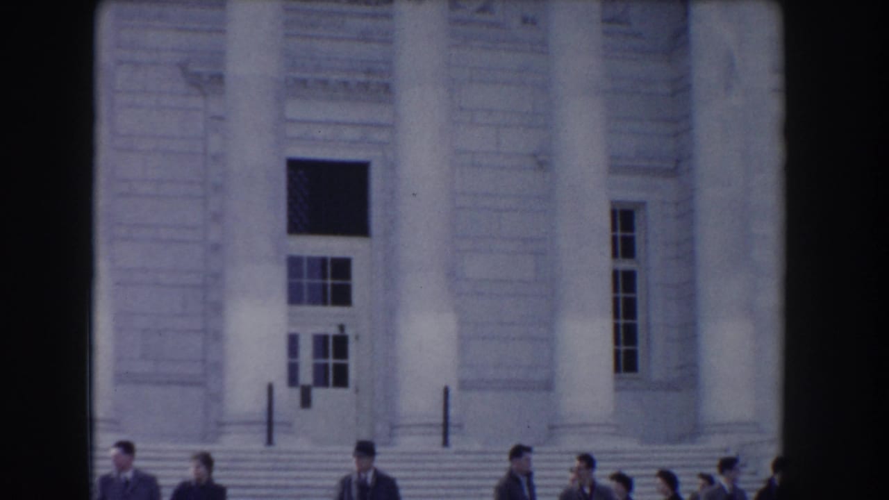 Neoclassical building entrance with columns and people passing along the lower edge.