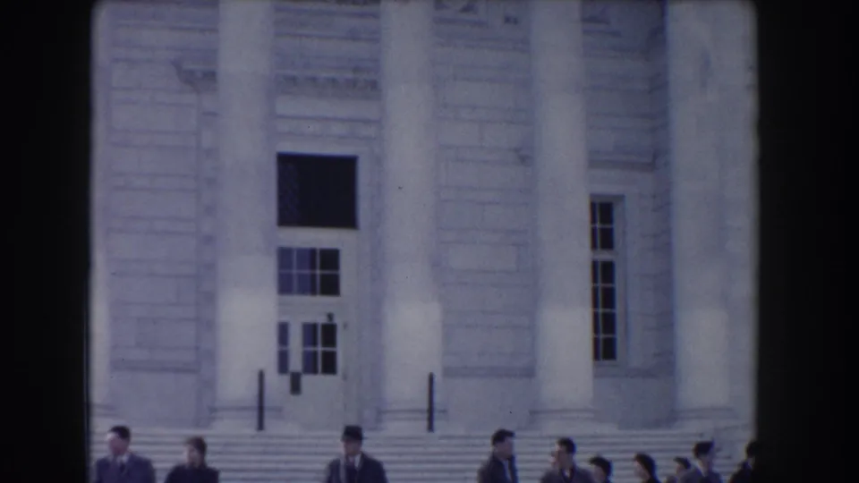 1960 Washington DC home-movie frame showing a columned neoclassical facade with civilians visible near the bottom of the shot.