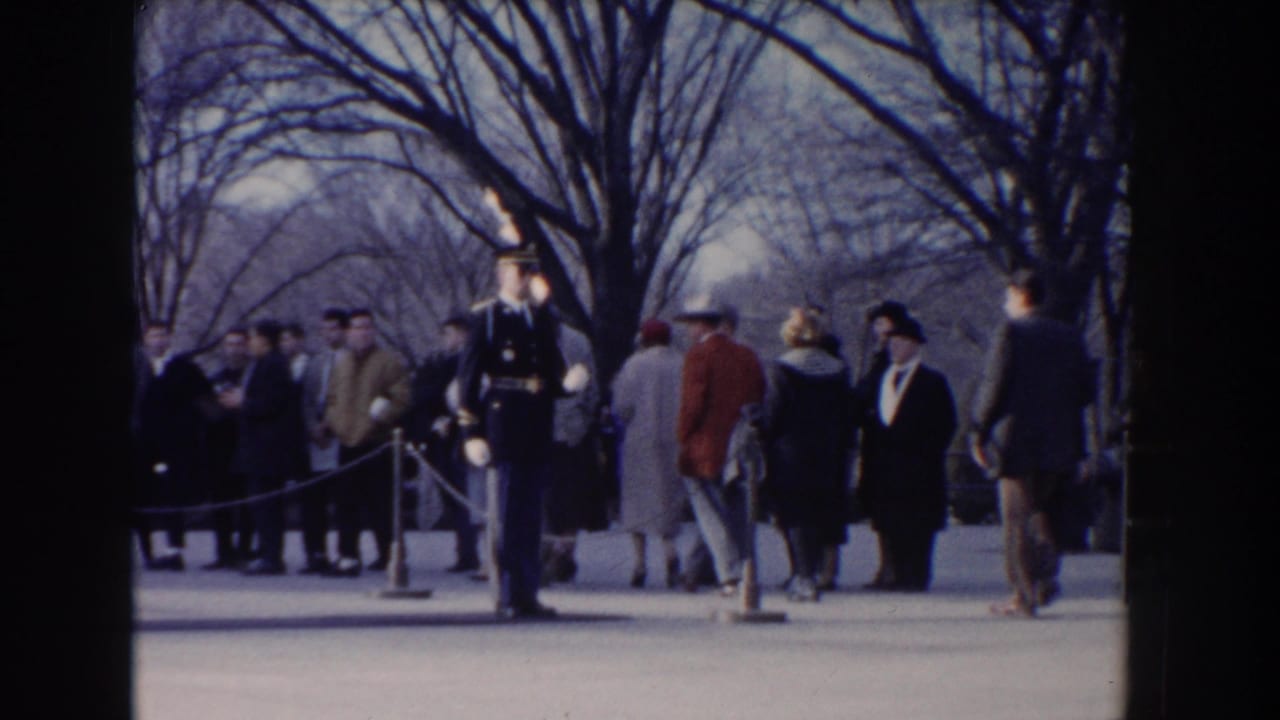 1960 Washington DC frame with a uniformed rifle-bearing guard standing before civilians gathered behind roped barriers.