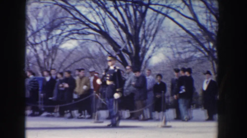 The 1960 Washington, DC home-movie frame shows a ceremonial guard near spectators and rope barriers beneath leafless trees.