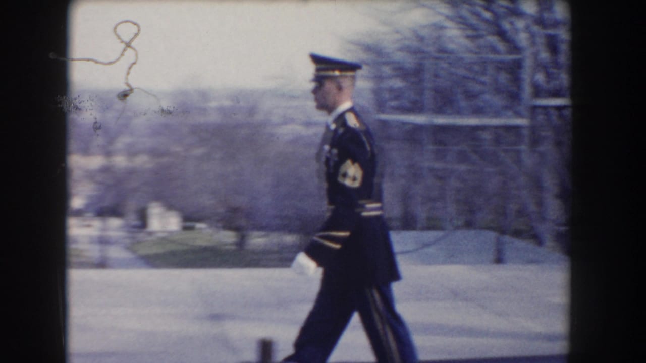Uniformed guard in profile marching beside a pale stone structure.