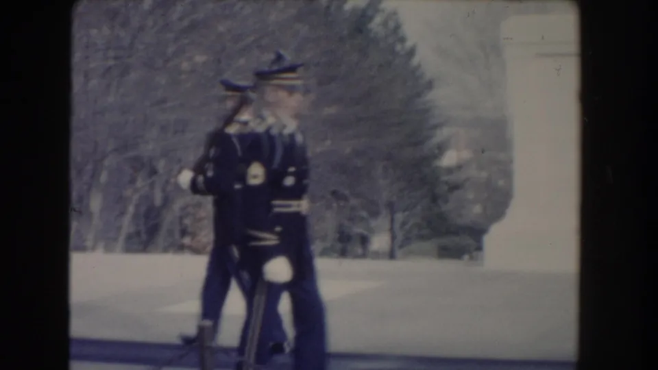 In 1960 Washington, DC footage, uniformed guards with rifles and white gloves march near a stone monument base.