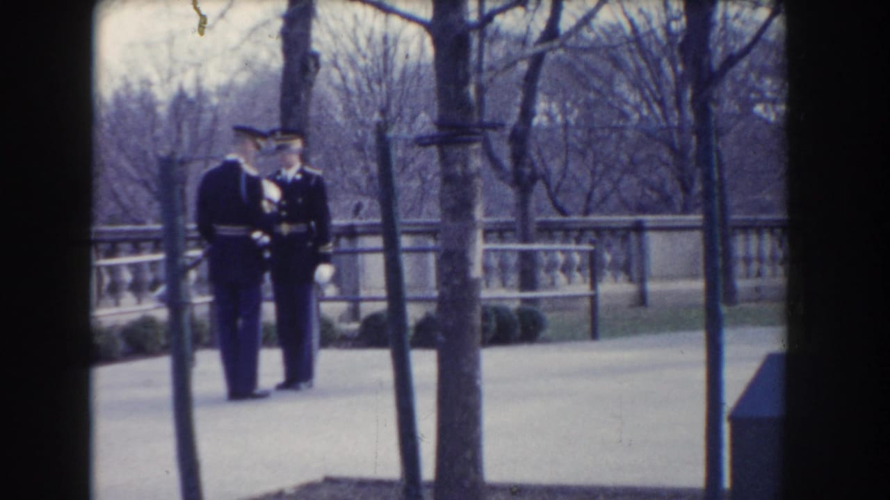 Two soldiers in dark uniforms face each other beside trees and a balustrade.