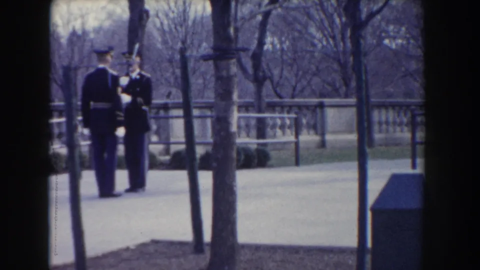Two uniformed soldiers stand close together during the guard ceremony, framed by trees and a stone balustrade in Washington, DC.
