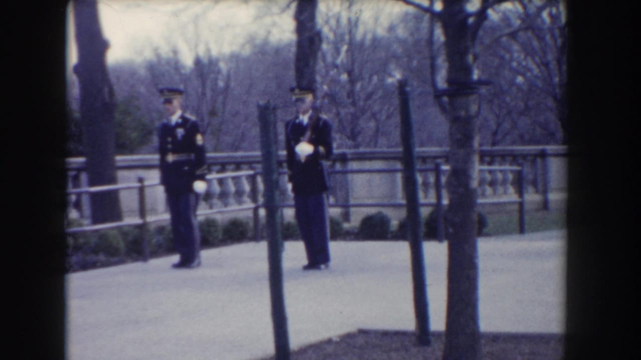 Two uniformed guards stand or begin marching on a paved path near a stone balustrade.