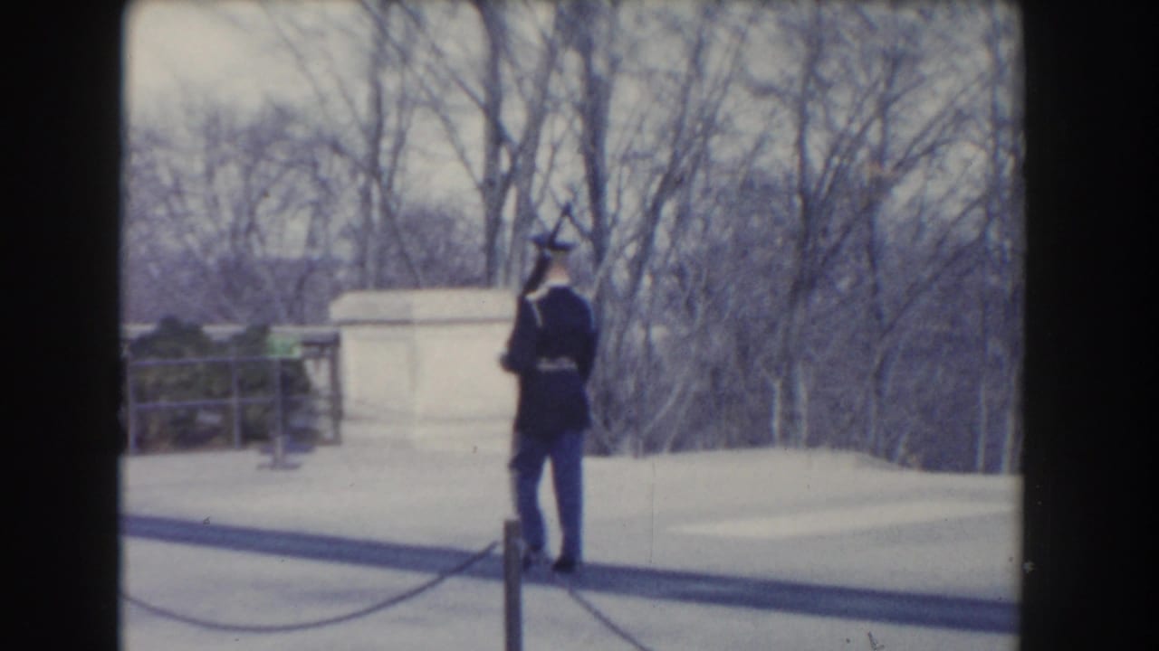 Uniformed guard standing near a white stone monument in snowy grounds.