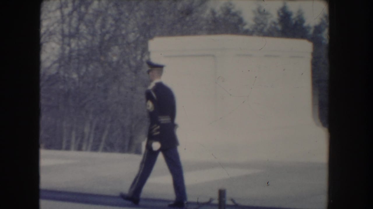 Uniformed guard walking beside a pale marble tomb structure.