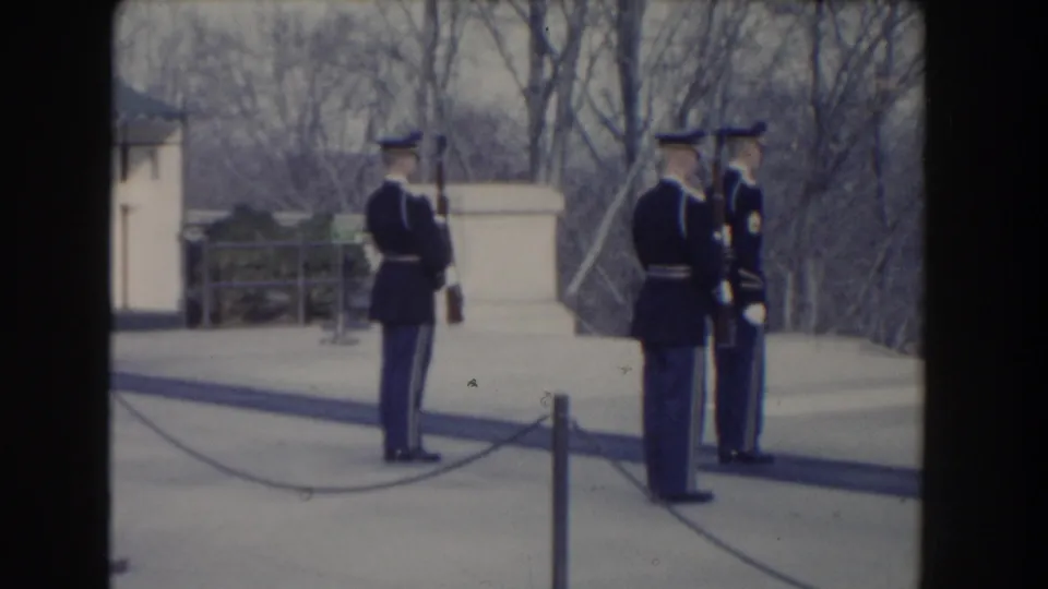 1960 Washington, DC frame showing uniformed guards positioned near the Tomb of the Unknown Soldier and public barrier.