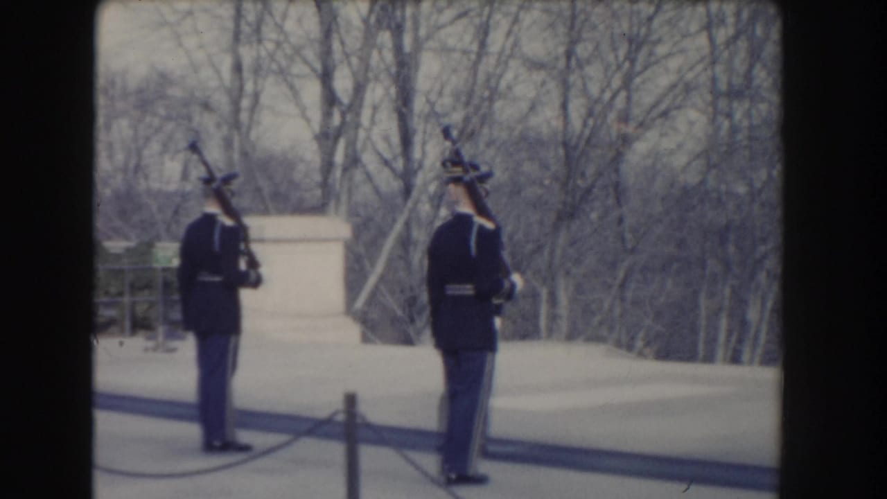 Two guards in dark uniforms hold rifles upright beside a pale stone structure.