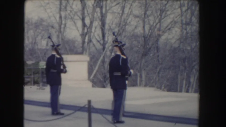 Washington, DC 1960 frame with two uniformed guards holding rifles upright against bare trees and light stonework.