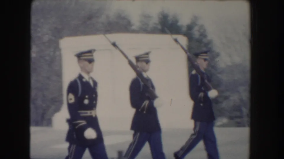 Three ceremonial guards march close to the camera, with a pale marble form and winter trees visible in the background.