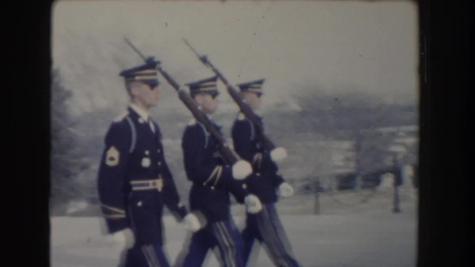 A close view shows the three uniformed guards marching together, with rifles, white gloves, and a distant landscape beyond the memorial grounds.
