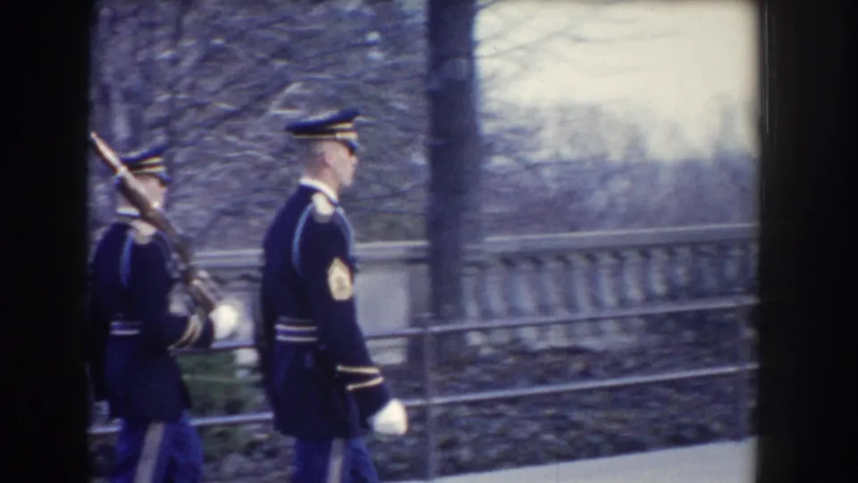 Two soldiers in formal uniforms march beside a stone balustrade, one carrying a rifle, in 1960 Washington DC 8mm footage.