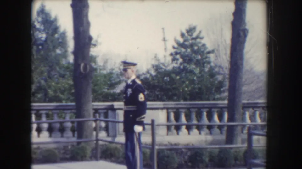 A single uniformed soldier is seen near a stone balustrade and trees in Washington DC ceremonial home-movie footage from 1960.