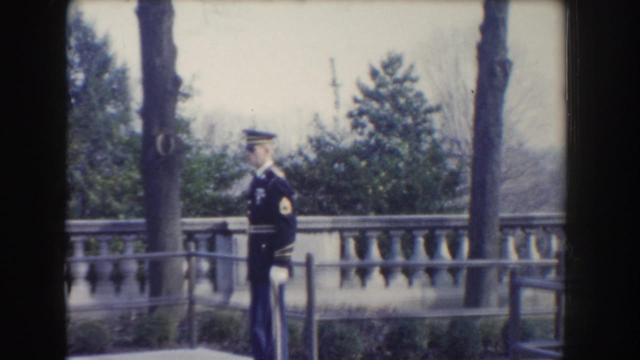 In Washington DC home-movie footage from 1960, a uniformed soldier stands at attention near a stone balustrade and trees.