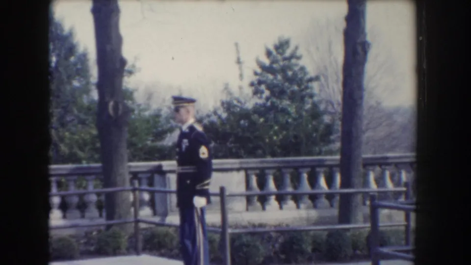A 1960 Washington DC frame shows a soldier standing at attention on a terrace, with trees and a stone railing behind him.