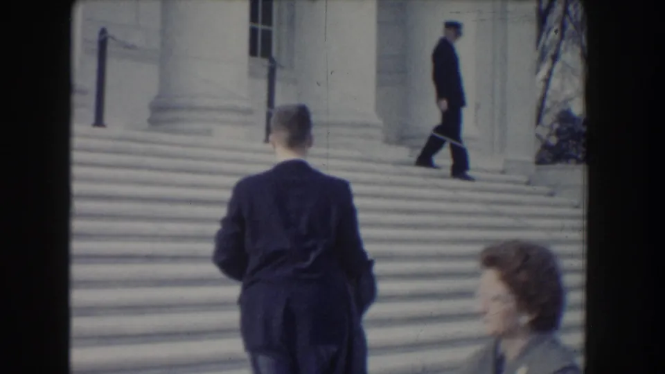 1960 Washington DC home-movie frame of suited pedestrians near the steps of a large stone civic building.