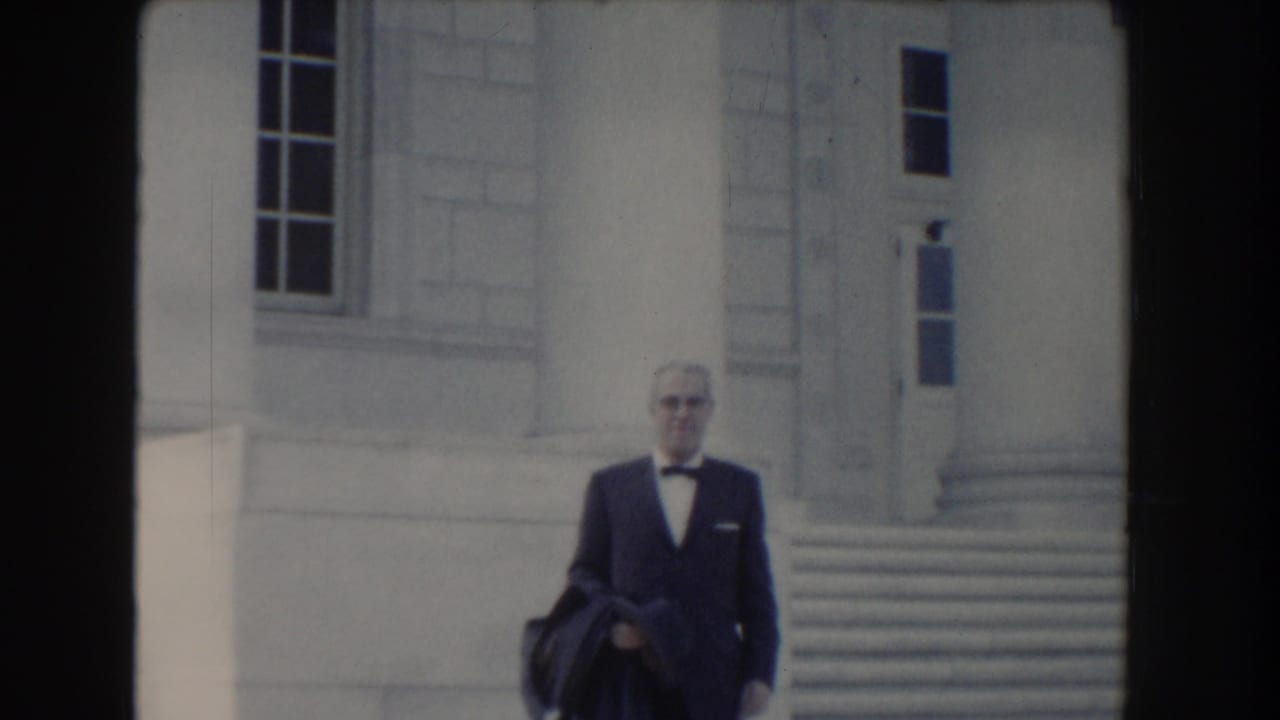 In 1960 Washington, DC footage, a suited man with a bow tie faces the camera near a classical stone building exterior.