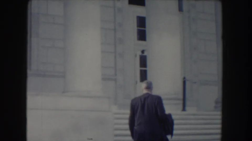 The suited figure is seen from behind as he approaches the steps of a grand stone building in 1960 Washington, DC footage.