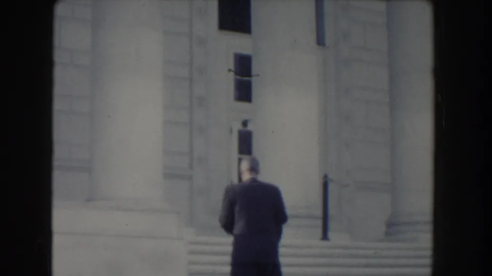 The man continues away from the camera toward the steps and columned facade, framed by the soft 8mm image.