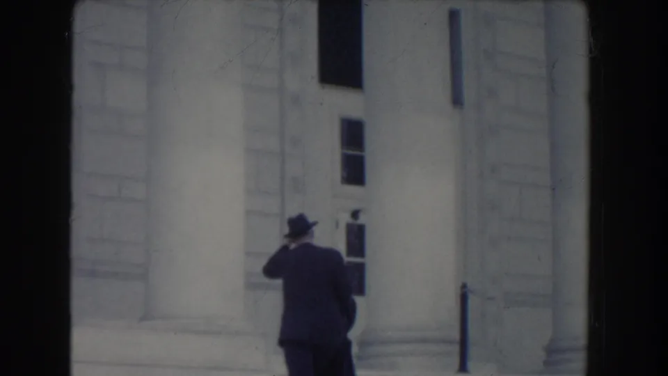A suited man seen from behind moves along the steps of a white columned building in Washington DC, 1960.