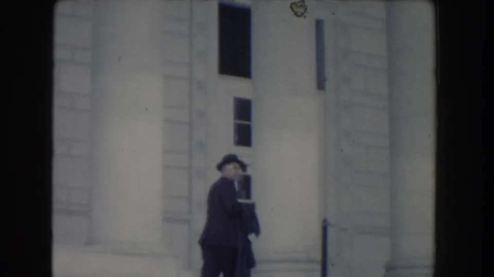 The man in a dark suit and hat turns partly toward the camera while standing near steps and columns in Washington DC, 1960.