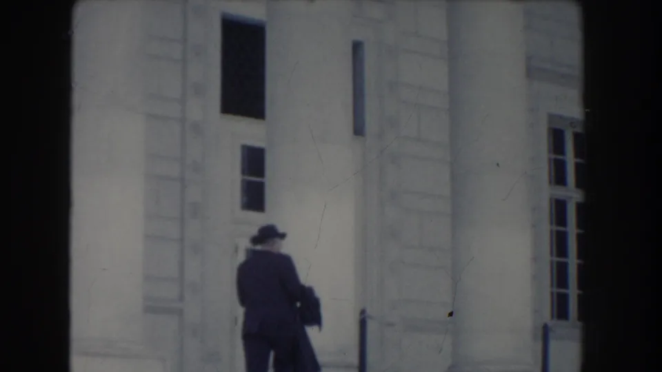 A suited man walks away near the steps and tall windows of a white columned building in Washington DC, 1960.