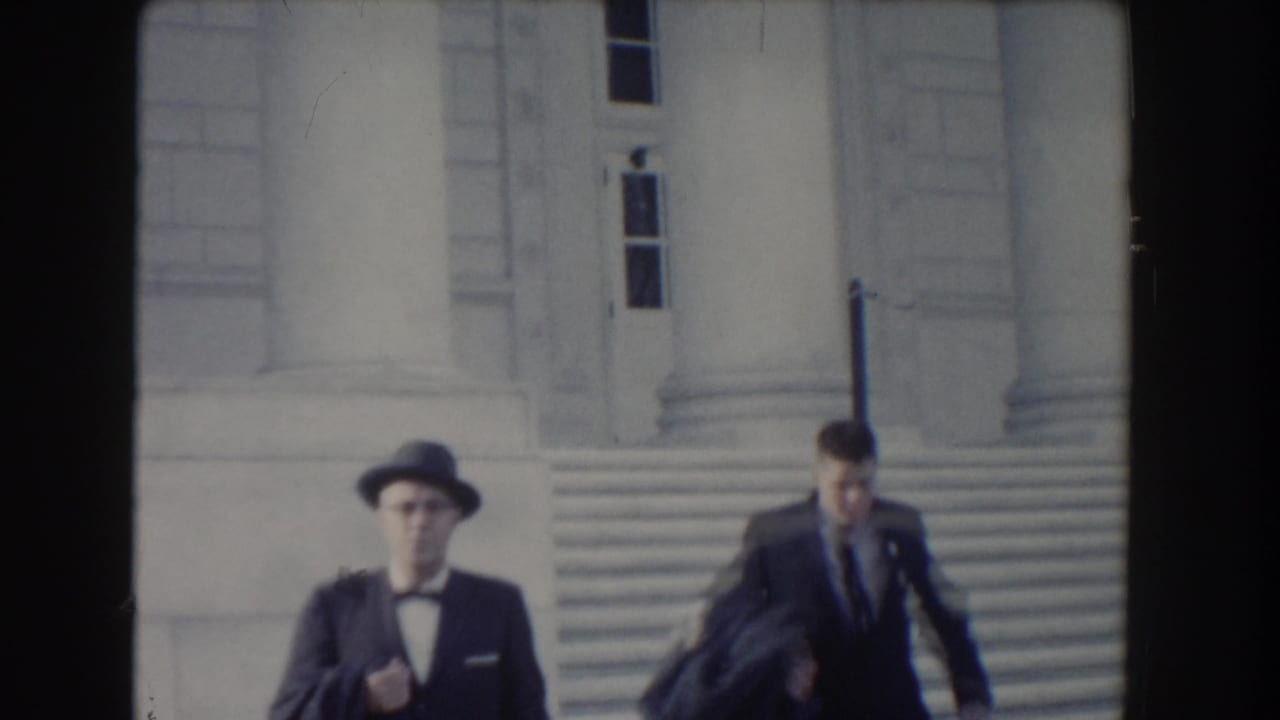 Two men in formal clothing move down stone steps in Washington, DC, one wearing a brimmed hat and bow tie.