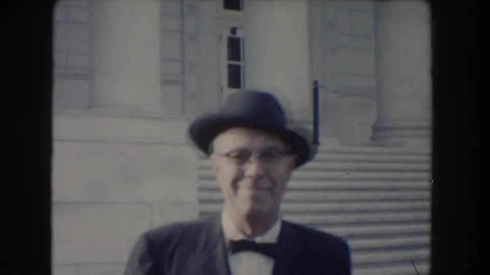Close view of a smiling man in glasses, bow tie, and brimmed hat with Washington, DC stone steps behind him.