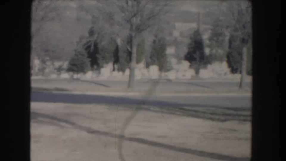 The 1960 home-movie view continues across cemetery grounds with white headstones, winter-bare trees, and soft 8mm color.