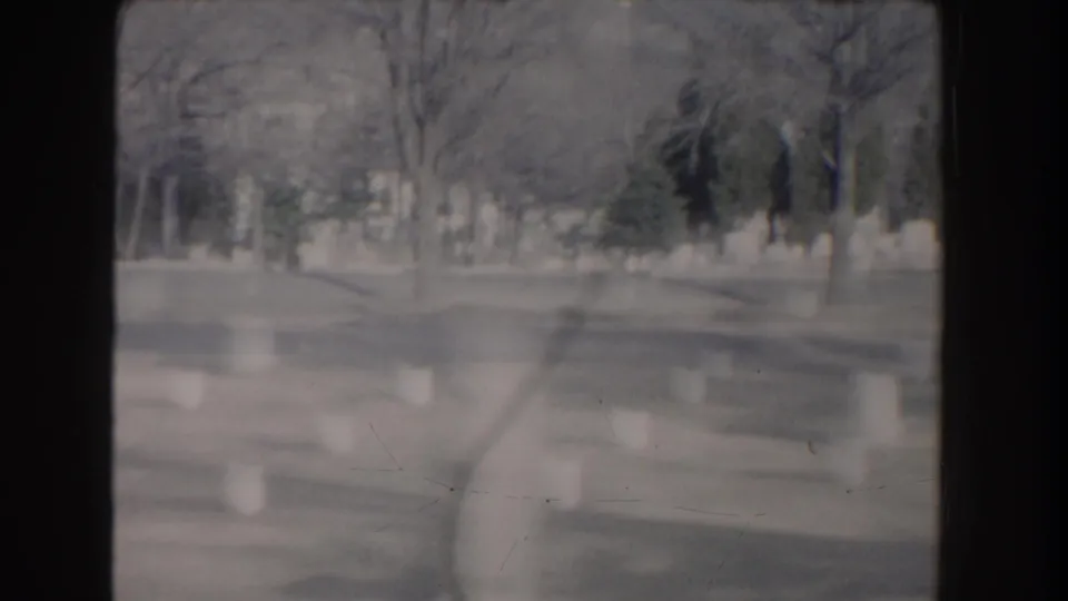 A soft, slightly blurred Washington, DC cemetery view shows headstones and trees framed by dark 8mm film borders.