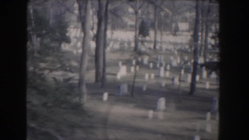 1960 8mm view of white cemetery headstones among bare trees in Washington, DC memorial grounds.