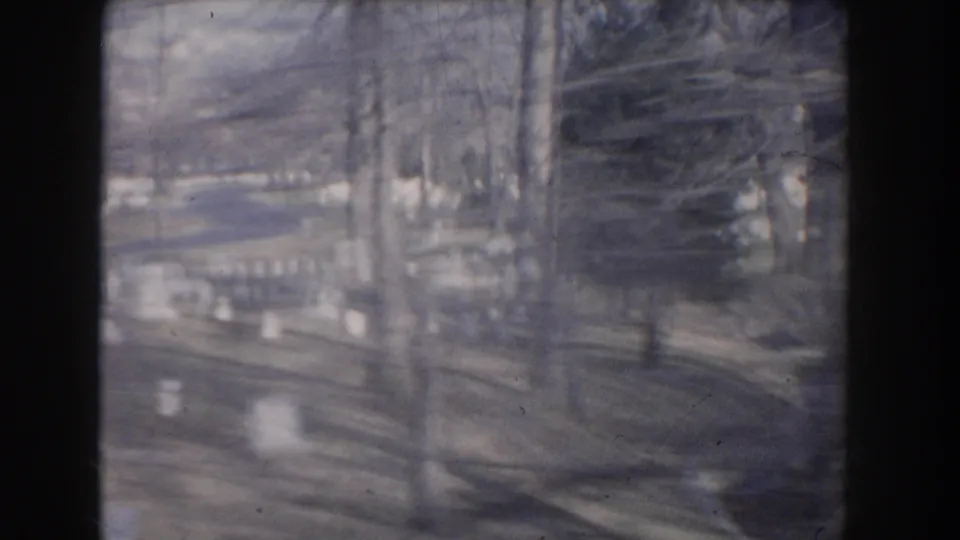 Passing 1960 8mm view of a cemetery road lined with white headstones and bare trees in Washington, DC.