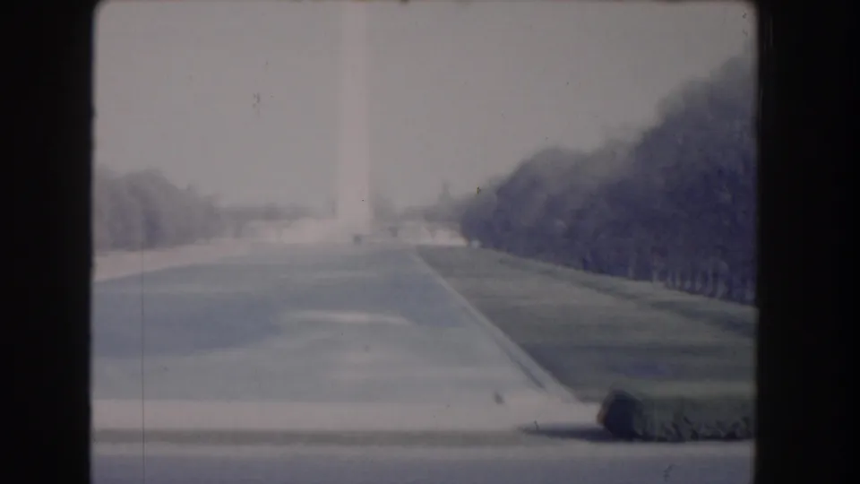 1960 Washington, DC home-movie frame looking toward the Washington Monument across open paths, lawns, and trees.