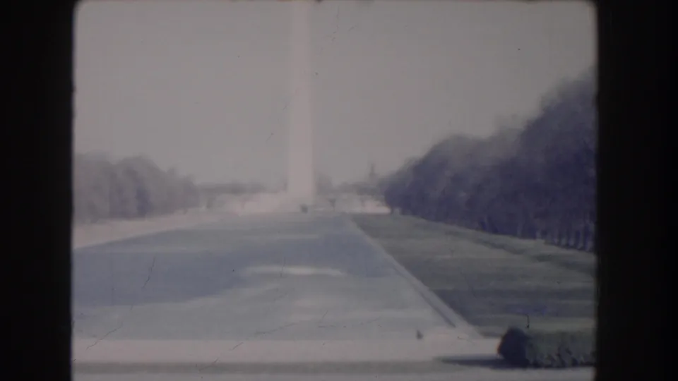 1960 Washington, DC frame showing the Washington Monument in the distance with tree-lined grounds and a small visitor figure.