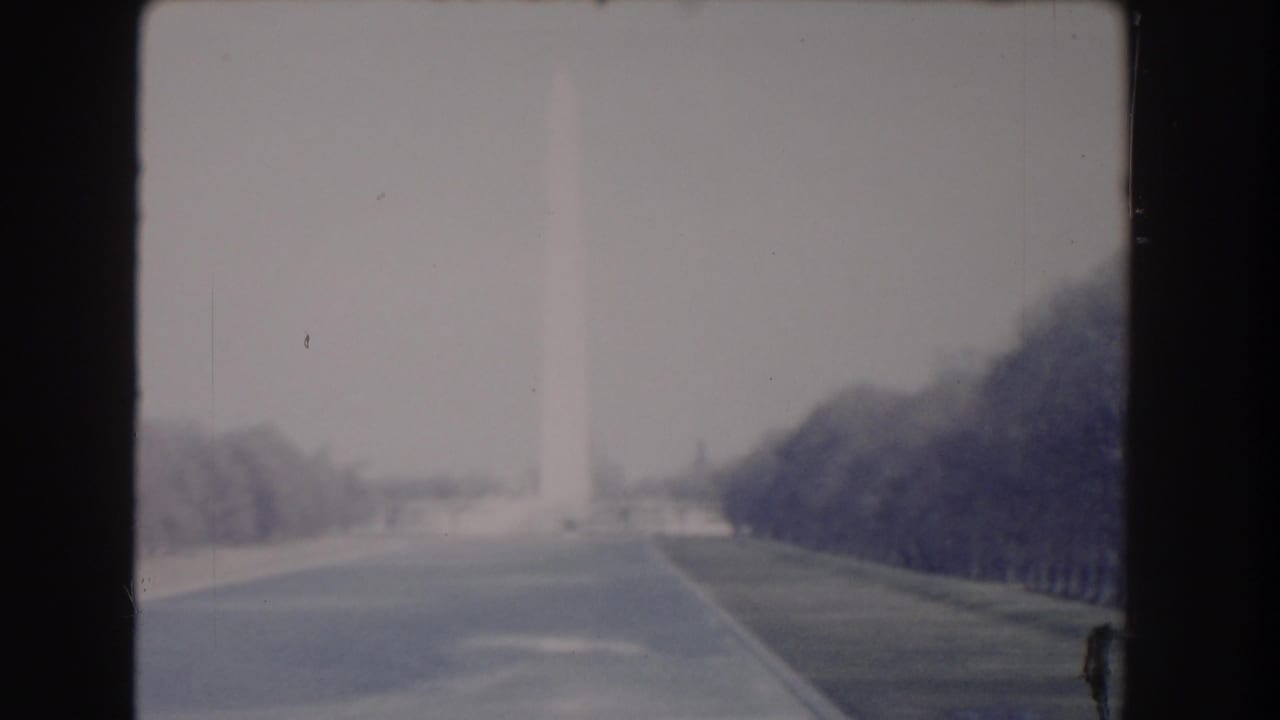 1960 Washington, DC frame with the Washington Monument barely visible through haze above a broad road and lawns.