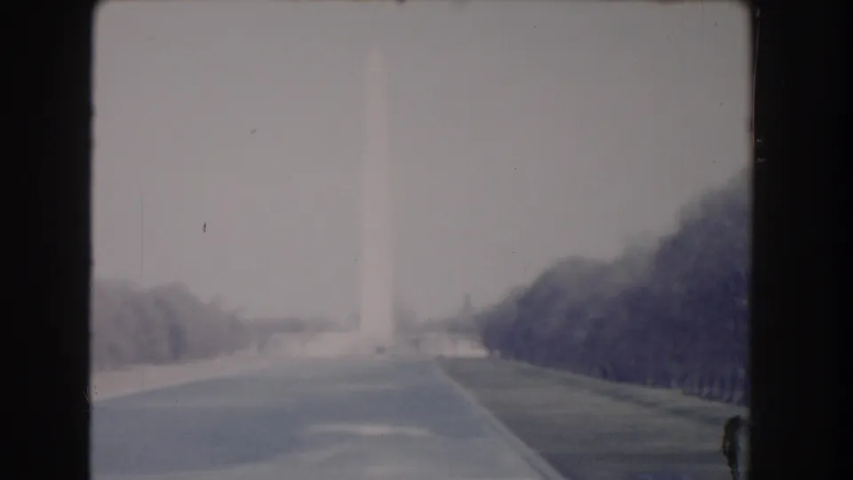 1960 Washington, DC frame with the Washington Monument barely visible through haze above a broad road and lawns.