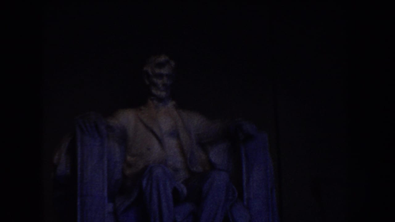 1960 8mm frame showing the Lincoln Memorial statue in Washington DC under dim blue-toned interior light.