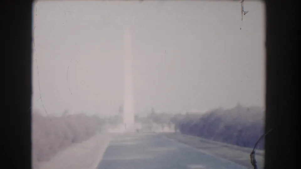 Overexposed 1960 Washington DC home-movie frame looking down a road or mall approach toward the distant Washington Monument.