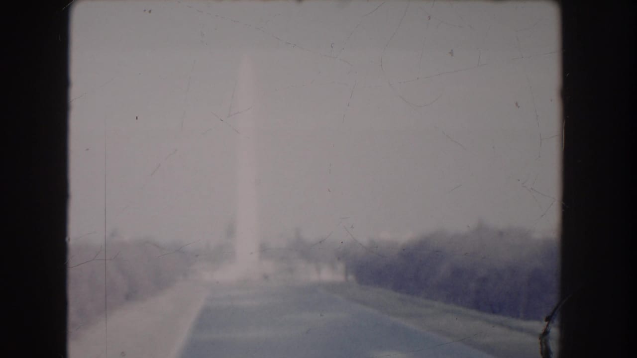 Soft 1960 8mm view in Washington, DC showing a hazy roadway leading toward a distant monument shape.