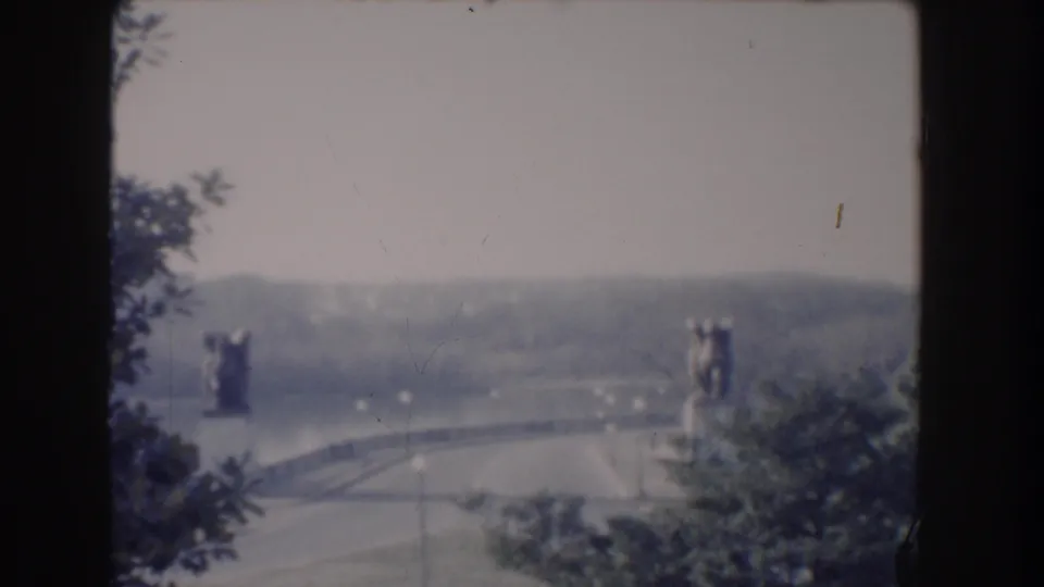 Elevated 1960 Washington, DC view of a curved bridge area flanked by large statues, with water and hills beyond.
