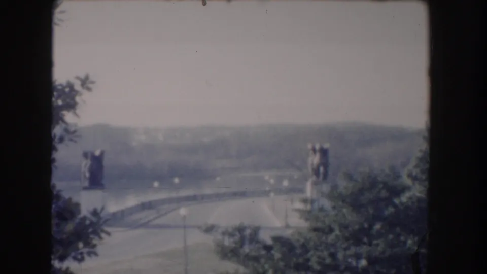 Wide 8mm Washington, DC landmark view with statue-flanked bridge, water, trees, and hazy hills in the distance.